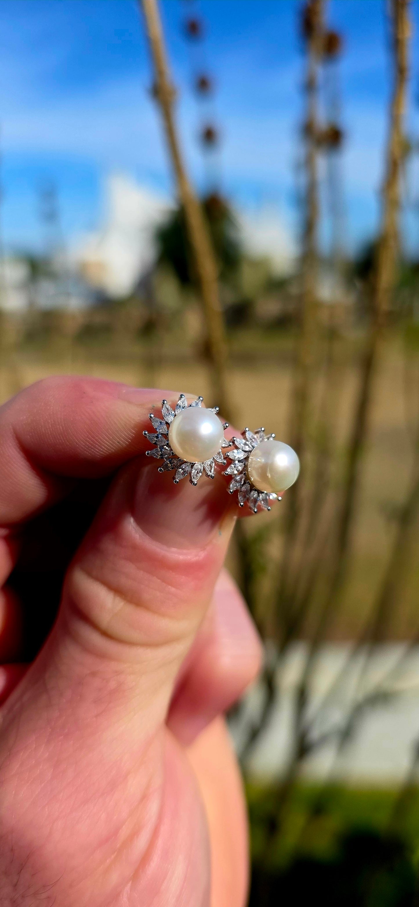 These elegant and beautifully classic sterling silver stud earrings each feature a luminous freshwater pearl at the centre, framed in a radiant halo of marquise-cut cubic zirconia gemstones in delicate prong settings.