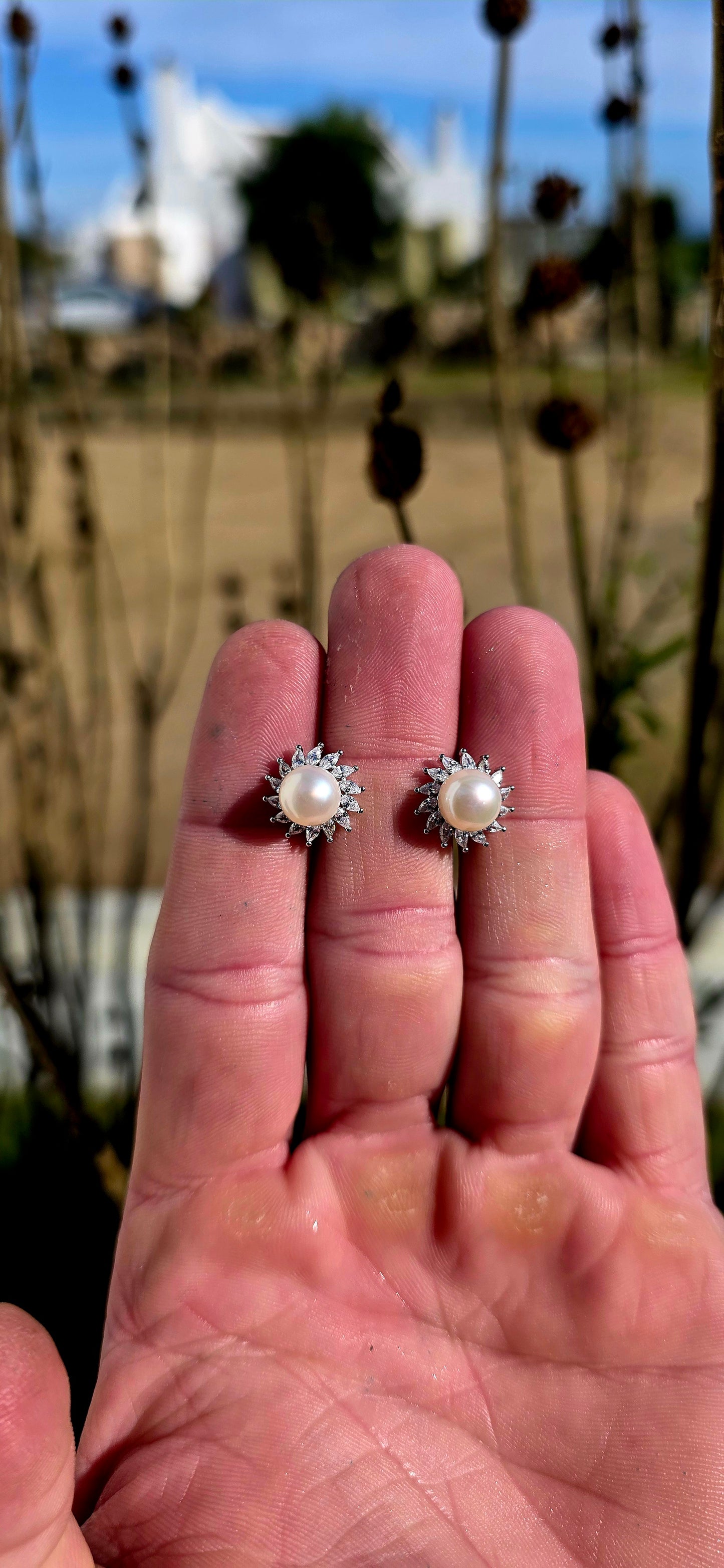 These elegant and beautifully classic sterling silver stud earrings each feature a luminous freshwater pearl at the centre, framed in a radiant halo of marquise-cut cubic zirconia gemstones in delicate prong settings.