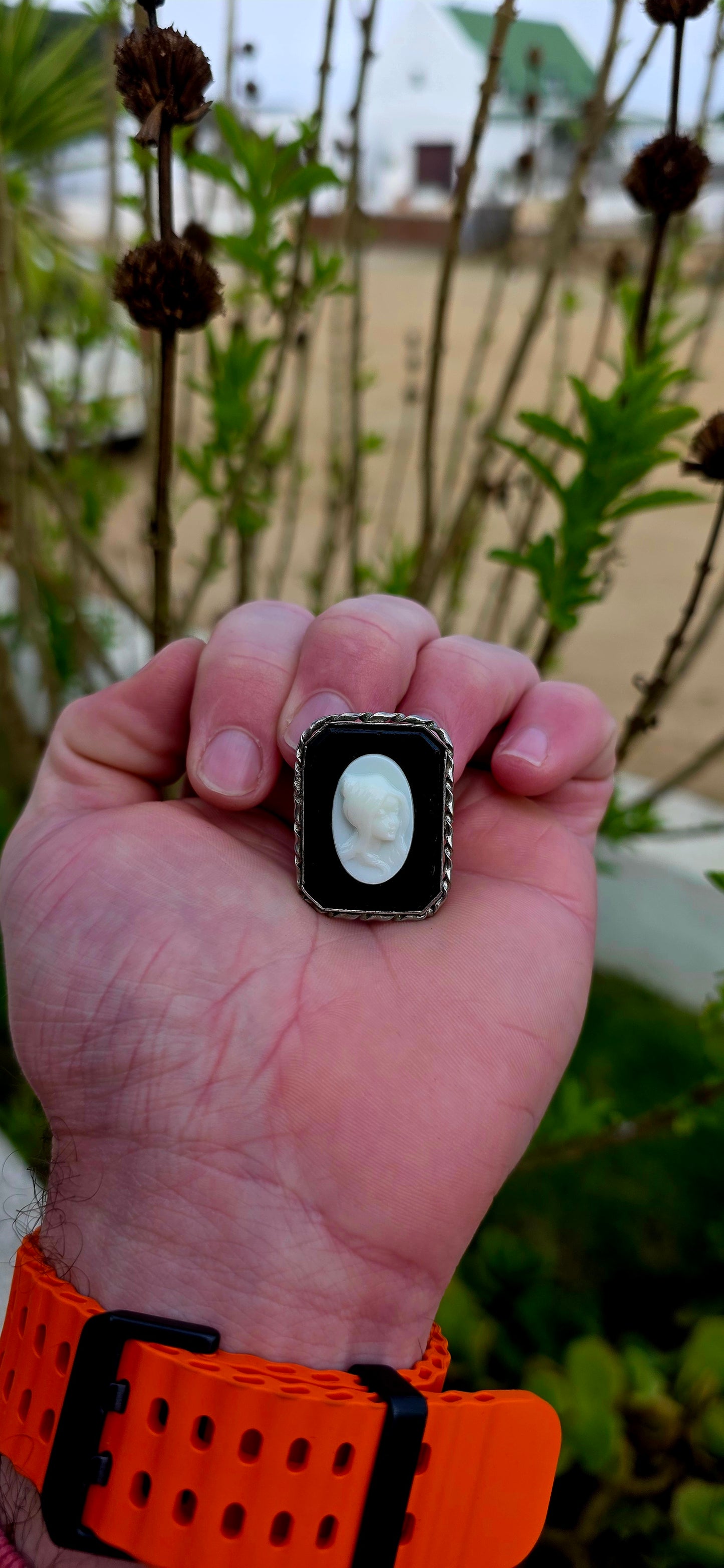 This beautiful vintage brooch features a striking oval milk glass cameo depicting the graceful profile of a young lady, her delicate features sculpted in crisp relief against a dramatic black glass background.