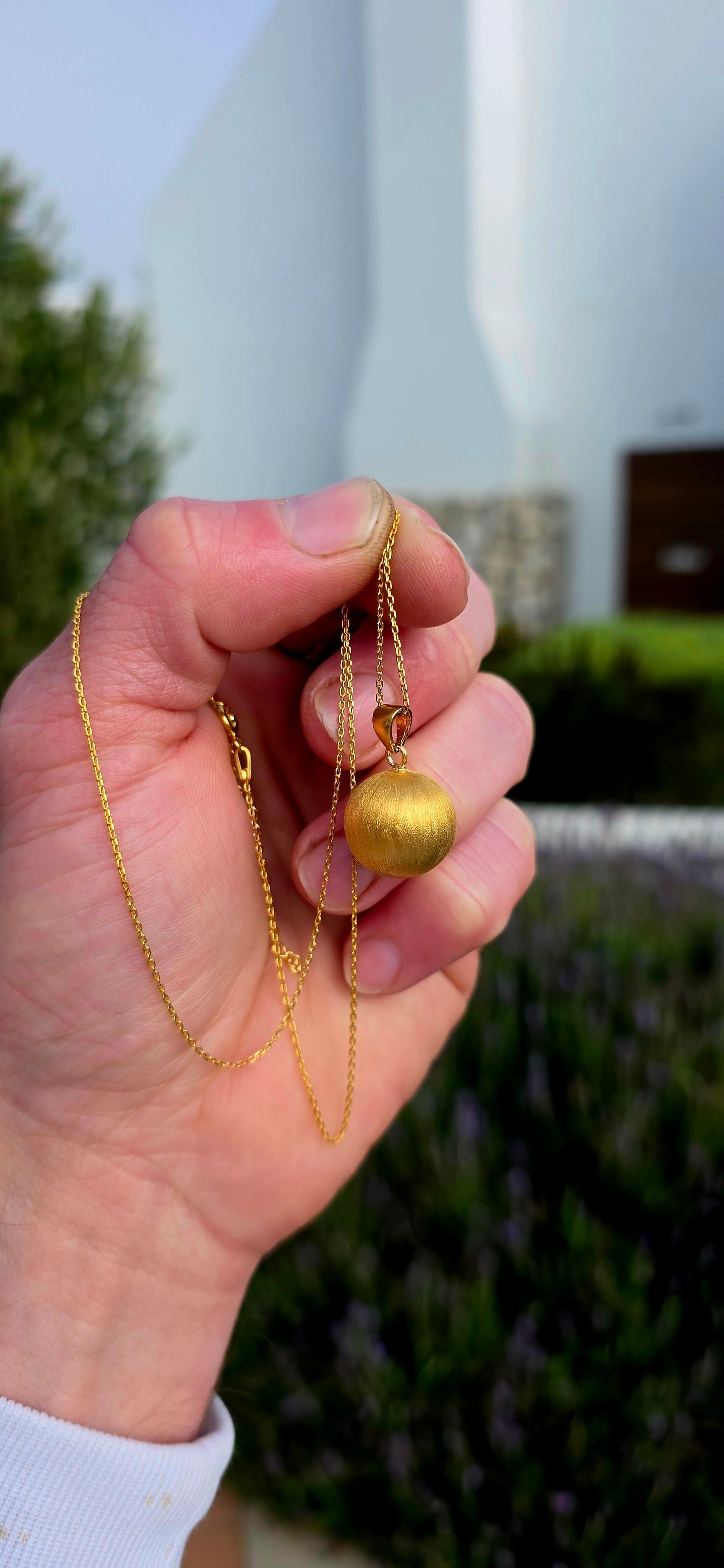 Crafted in sterling silver and finished with a luxurious layer of 18ct yellow gold plating, this striking pendant features a beautifully textured spherical orb with a soft satin finish that catches the light with a warm golden glow.