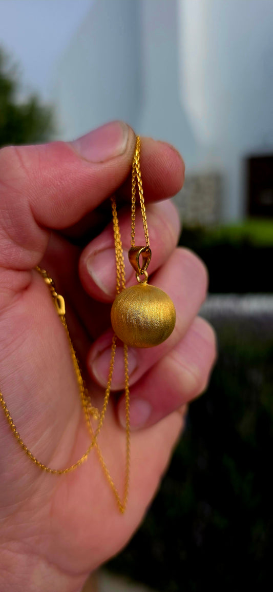 Crafted in sterling silver and finished with a luxurious layer of 18ct yellow gold plating, this striking pendant features a beautifully textured spherical orb with a soft satin finish that catches the light with a warm golden glow.