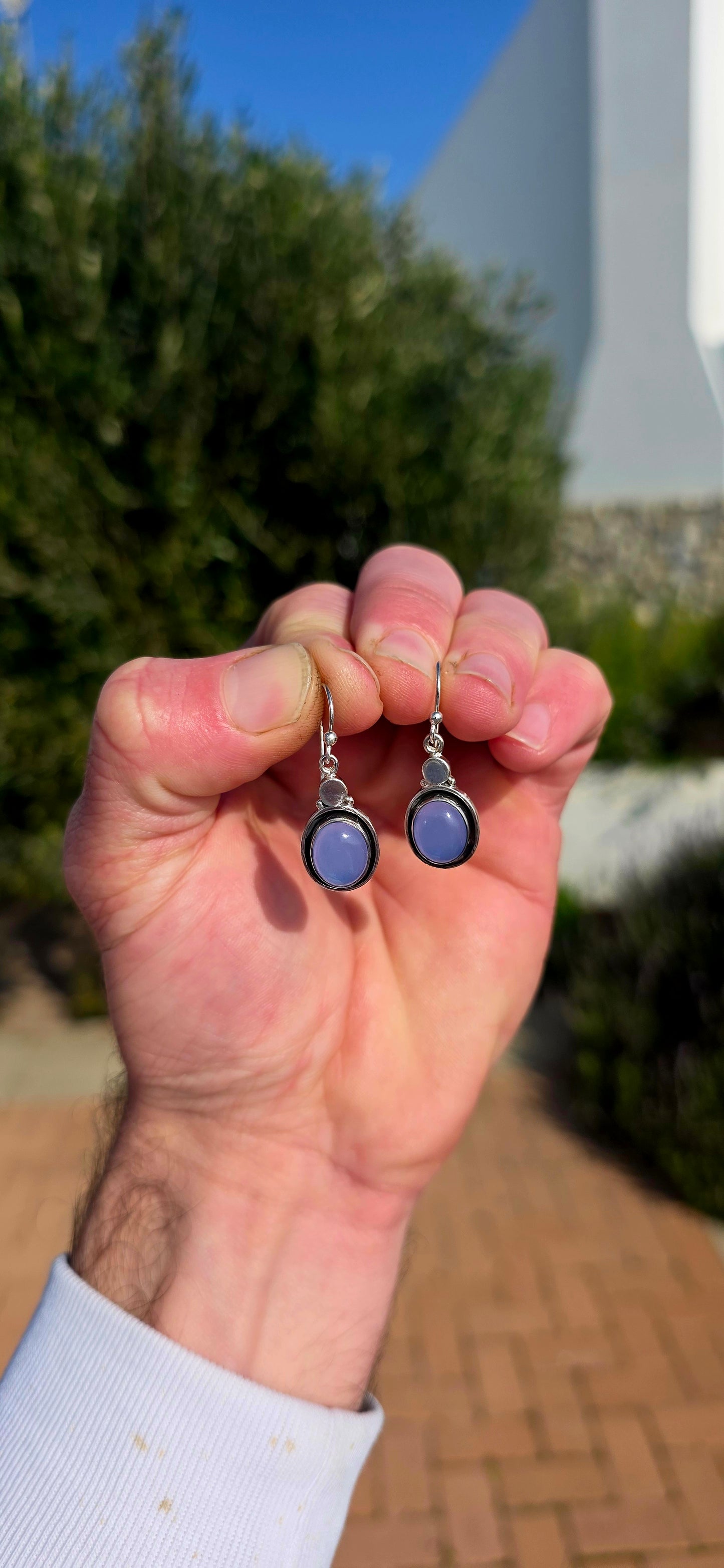 This artisan-made pair of sterling silver drop earrings features smooth, oval lavender-blue chalcedony cabochons, each beautifully tube-set in polished silver.