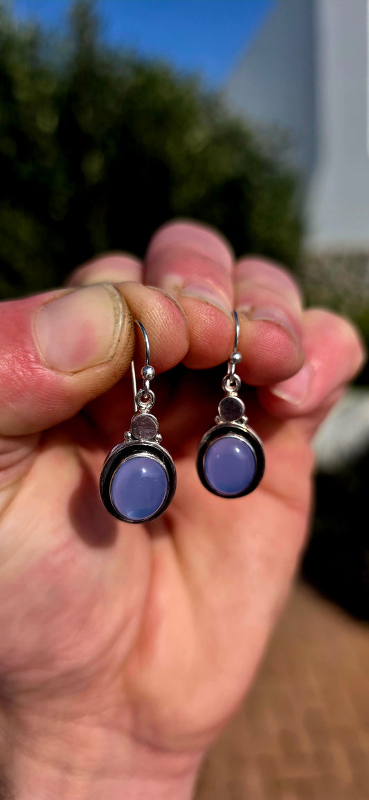 This artisan-made pair of sterling silver drop earrings features smooth, oval lavender-blue chalcedony cabochons, each beautifully tube-set in polished silver.