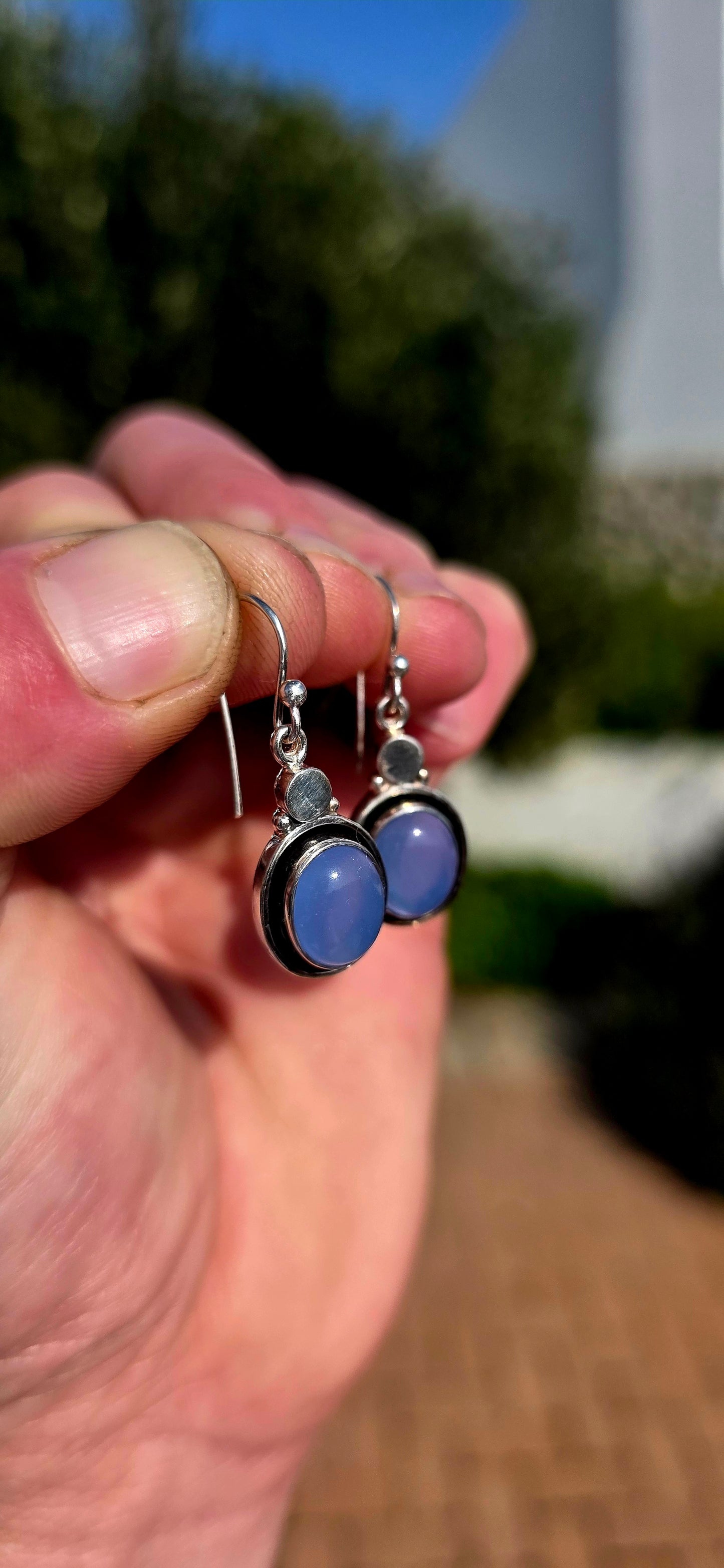 This artisan-made pair of sterling silver drop earrings features smooth, oval lavender-blue chalcedony cabochons, each beautifully tube-set in polished silver.