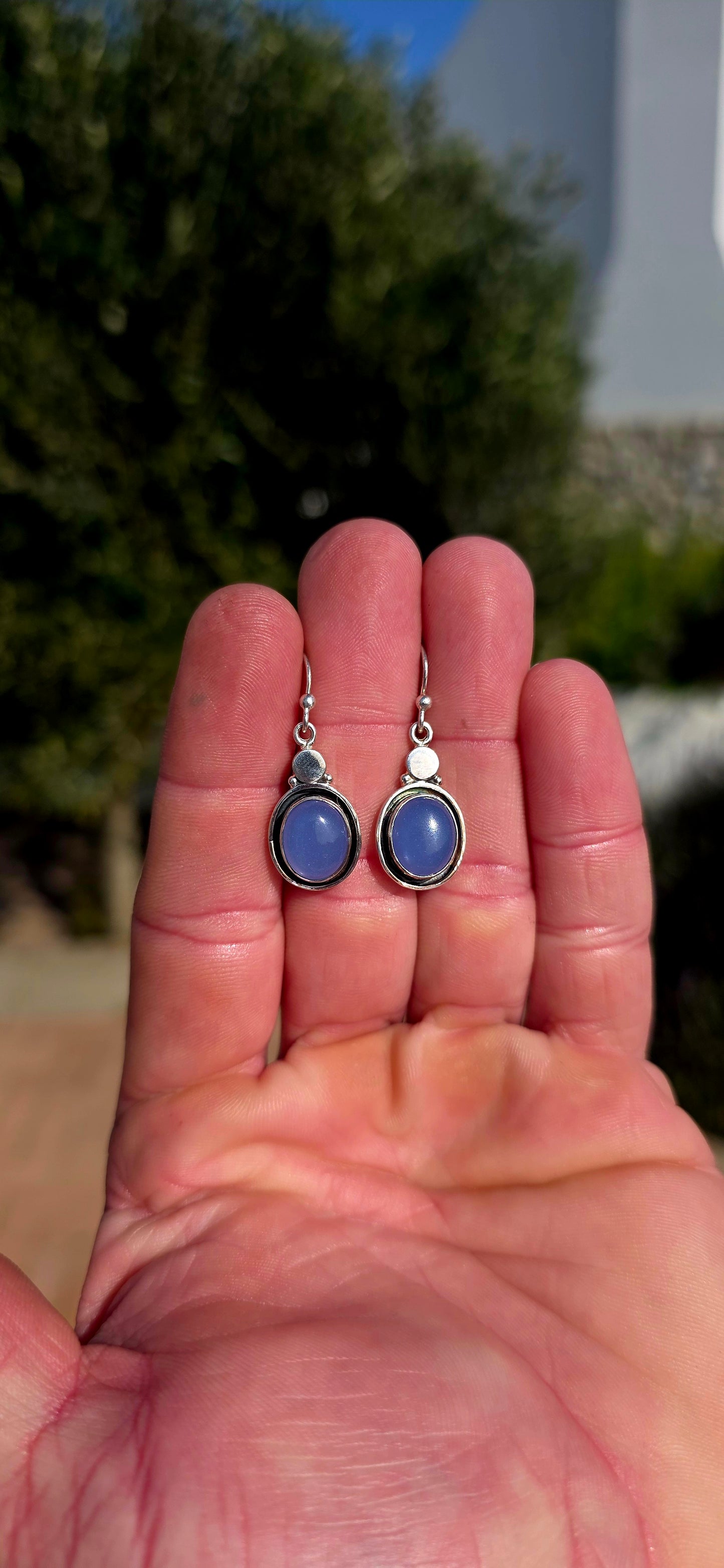 This artisan-made pair of sterling silver drop earrings features smooth, oval lavender-blue chalcedony cabochons, each beautifully tube-set in polished silver.