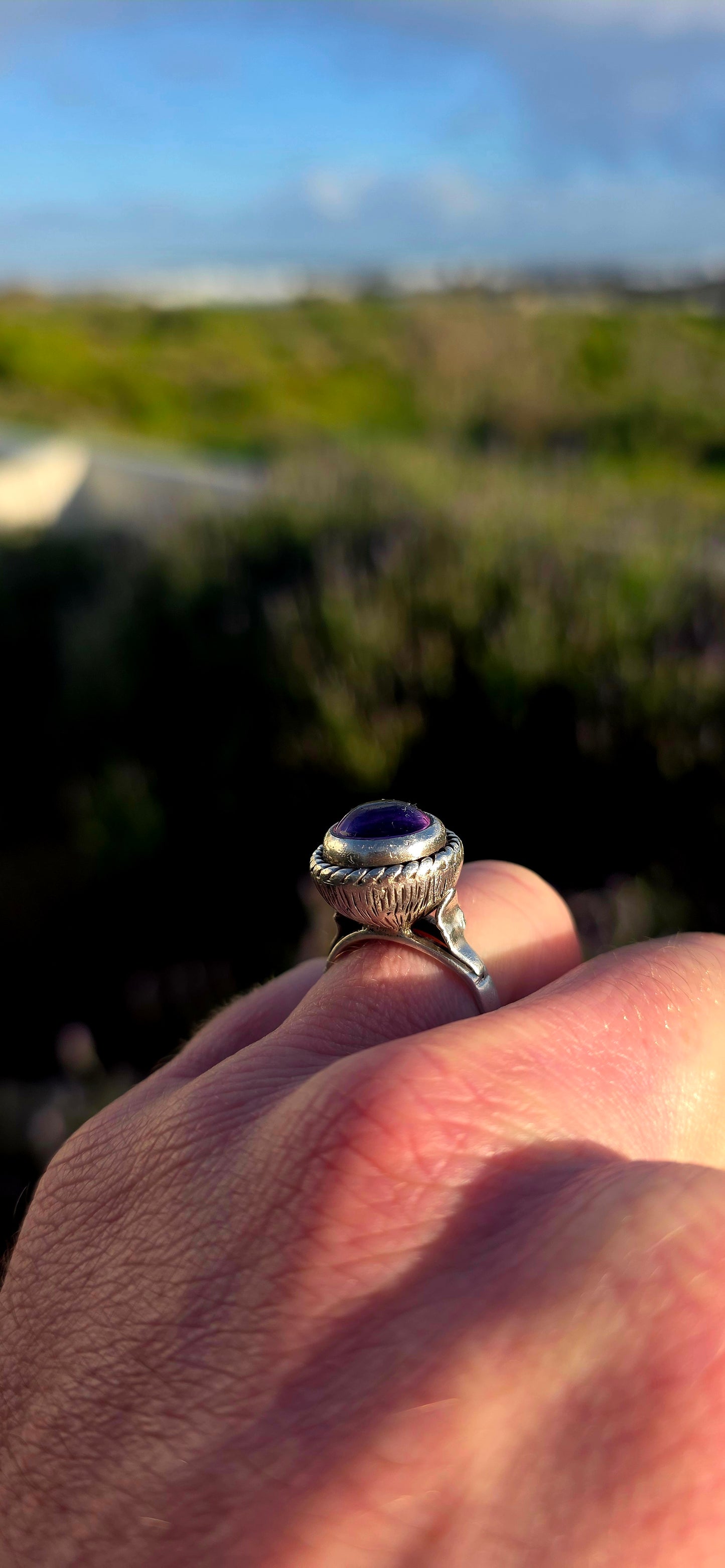 This striking handcrafted Kabwe sterling silver ring features a glowing rounded amethyst cabochon, elegantly tube-set within a beautifully raised and richly textured domed setting.