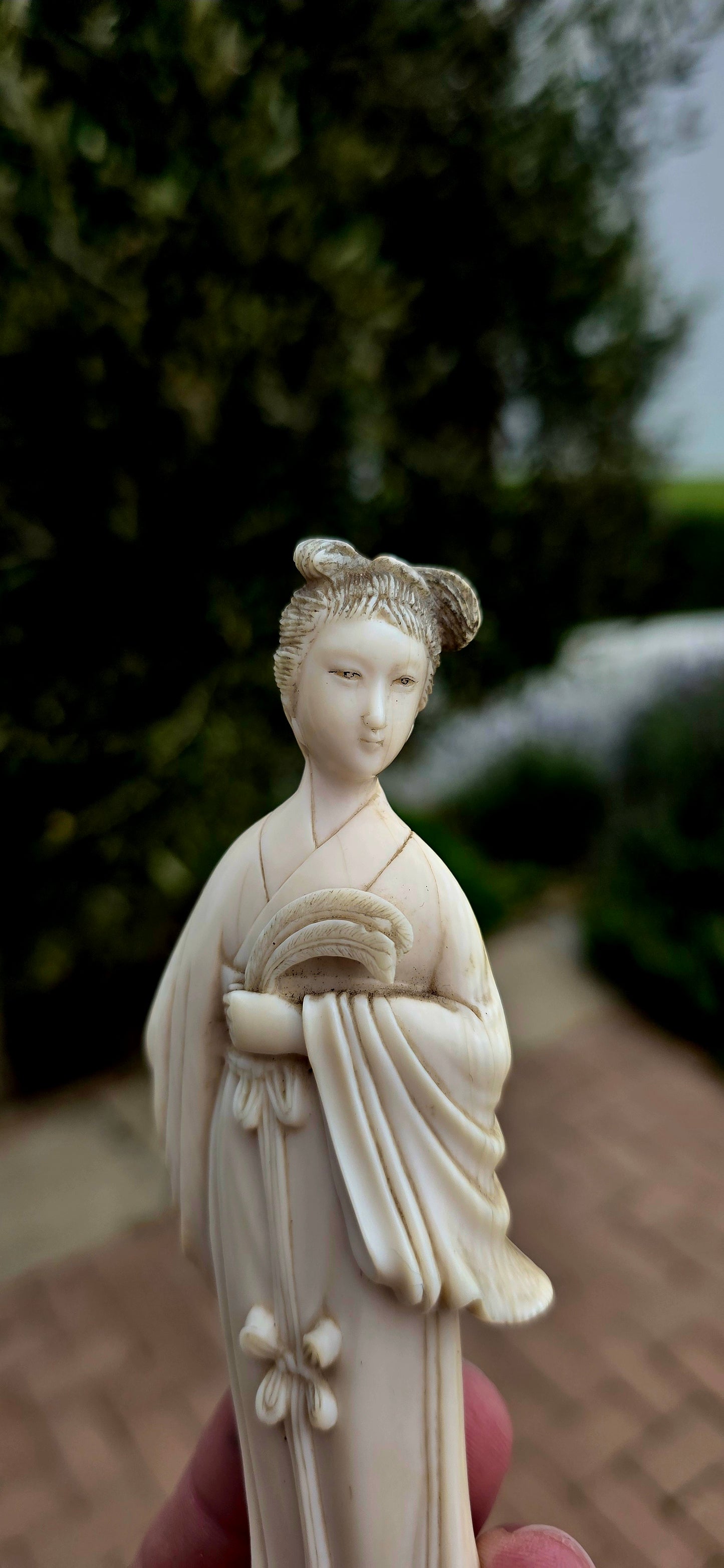 A wonderfully refined 19th-century hand-carved Japanese ivory sculpture, depicting a graceful Bijin (meaning "beautiful woman") elegantly dressed in flowing traditional robes and delicately holding an uchiwa (rigid ceremonial fan).
