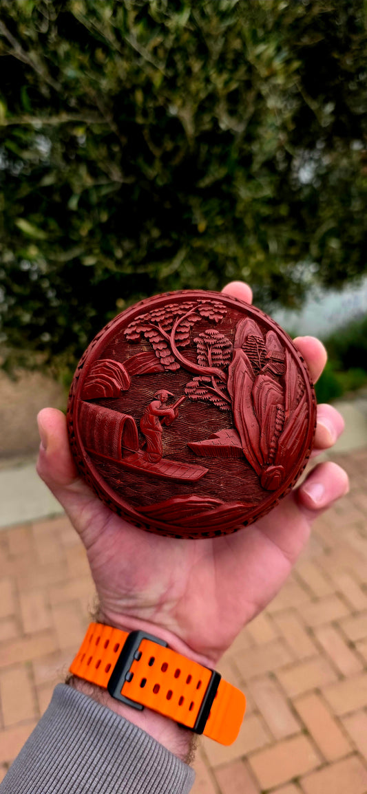 A magnificent Chinese cloisonné enamel and carved cinnabar circular box and lid, beautifully decorated with a tranquil riverside landscape depicting a lone scholar crossing the water toward towering mountains and a secluded pavilion.