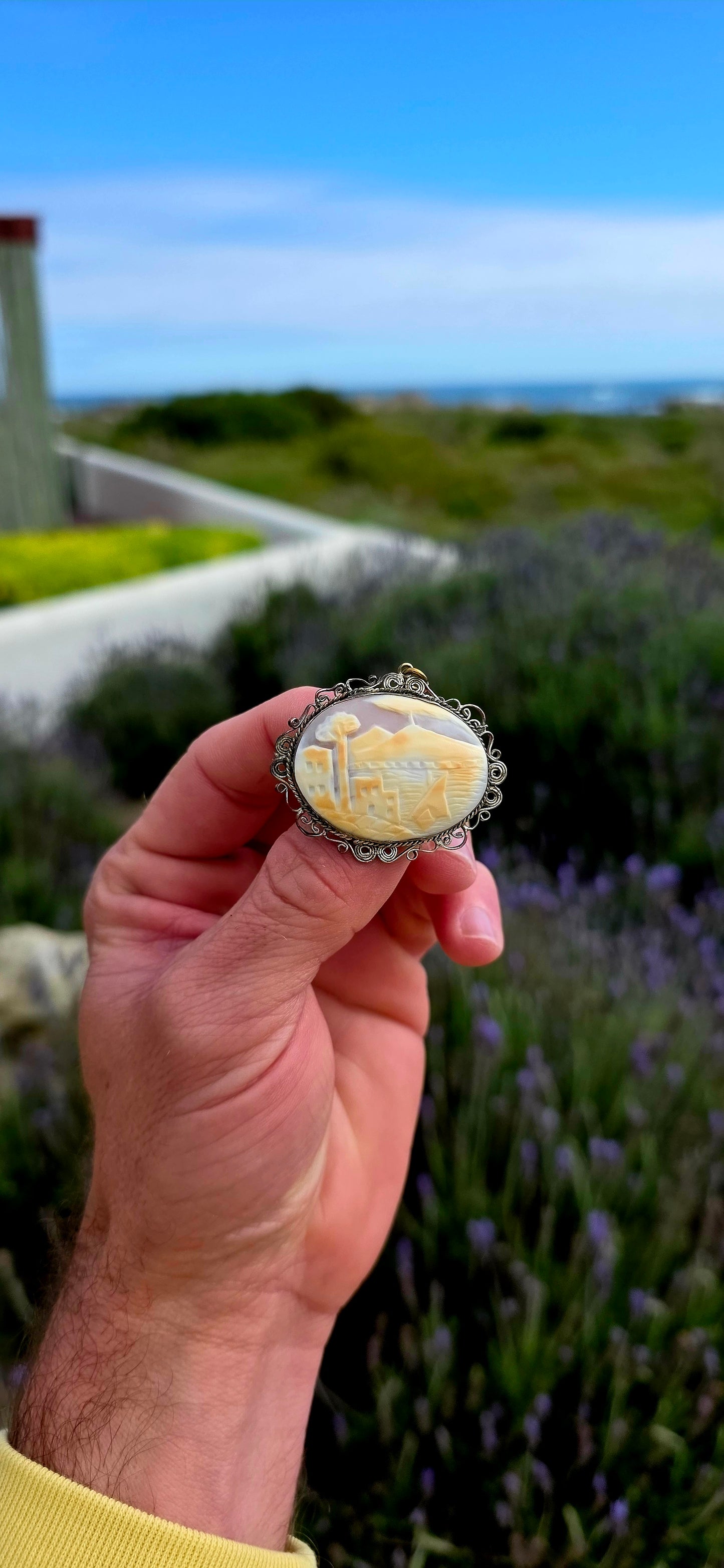 Beautifully handcrafted, this vintage silver-plated filigree cameo features a finely hand-carved conch shell depicting a tranquil coastal village scene.