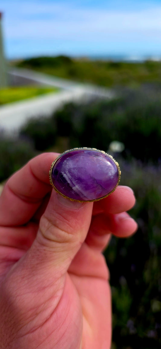 A truly beautiful antique treasure, this 10ct yellow gold brooch showcases a generously sized natural oval amethyst cabochon, celebrated for its rich royal-purple hues and soft, glowing lustre.