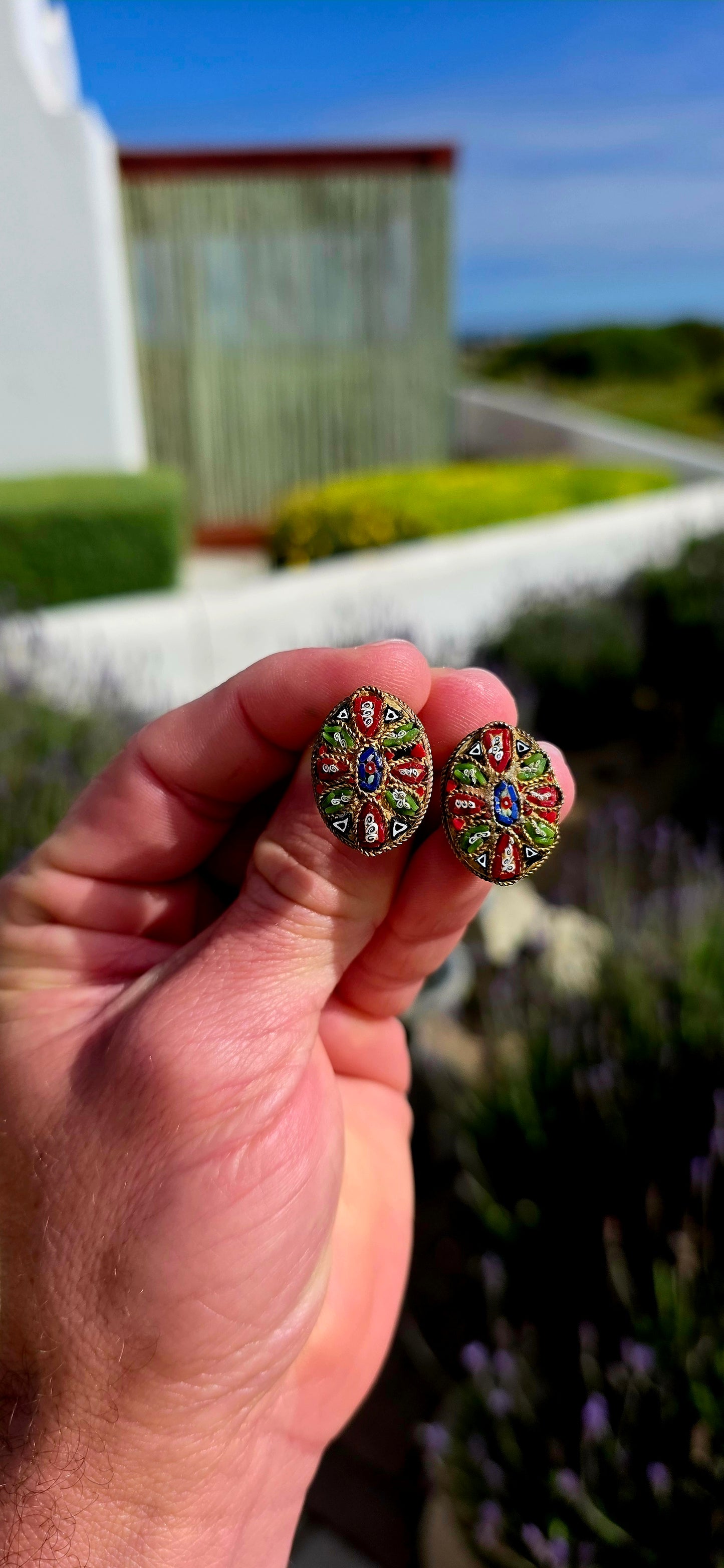 A charming pair of antique oval micro mosaic clip-on earrings, beautifully handcrafted using hundreds of individually placed glass tesserae to create intricate floral and geometric patterns in vibrant shades of red, blue, green, white and black.