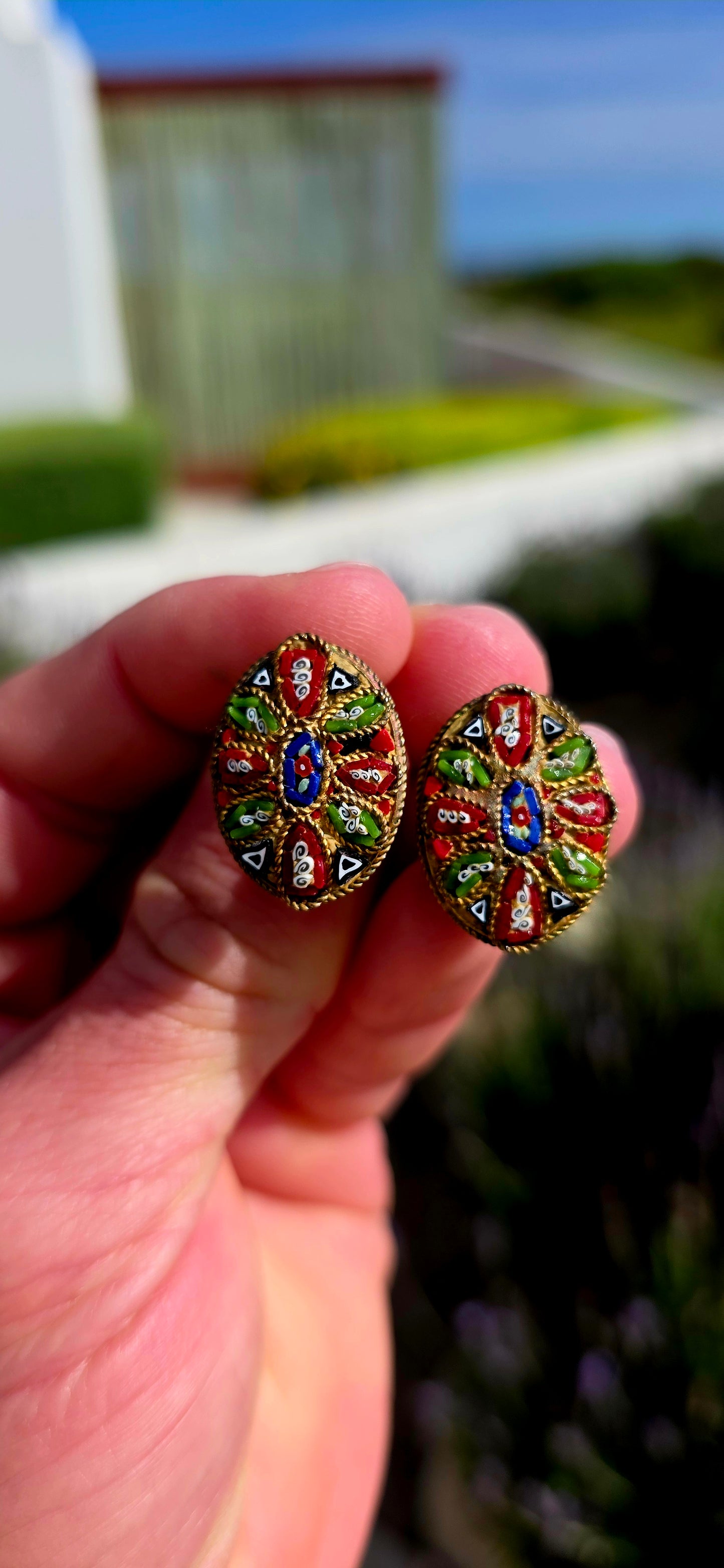 A charming pair of antique oval micro mosaic clip-on earrings, beautifully handcrafted using hundreds of individually placed glass tesserae to create intricate floral and geometric patterns in vibrant shades of red, blue, green, white and black.