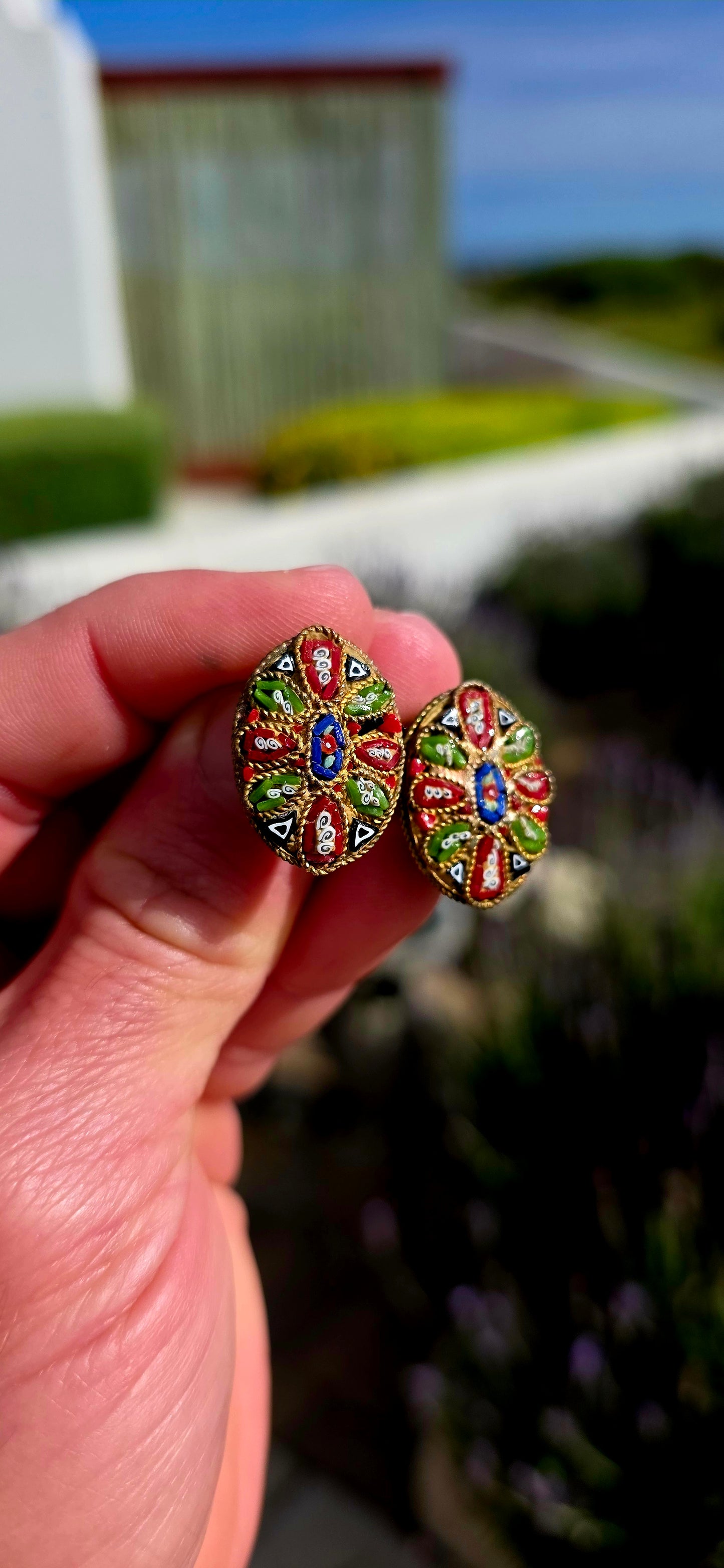 A charming pair of antique oval micro mosaic clip-on earrings, beautifully handcrafted using hundreds of individually placed glass tesserae to create intricate floral and geometric patterns in vibrant shades of red, blue, green, white and black.