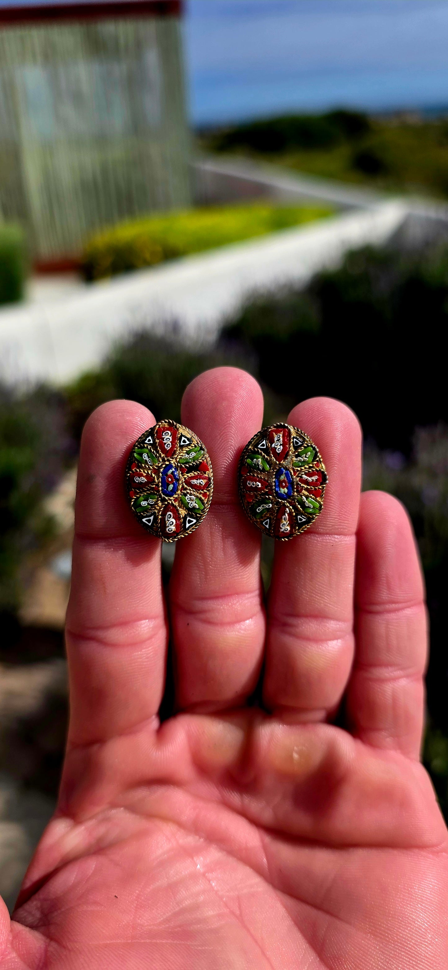 A charming pair of antique oval micro mosaic clip-on earrings, beautifully handcrafted using hundreds of individually placed glass tesserae to create intricate floral and geometric patterns in vibrant shades of red, blue, green, white and black.