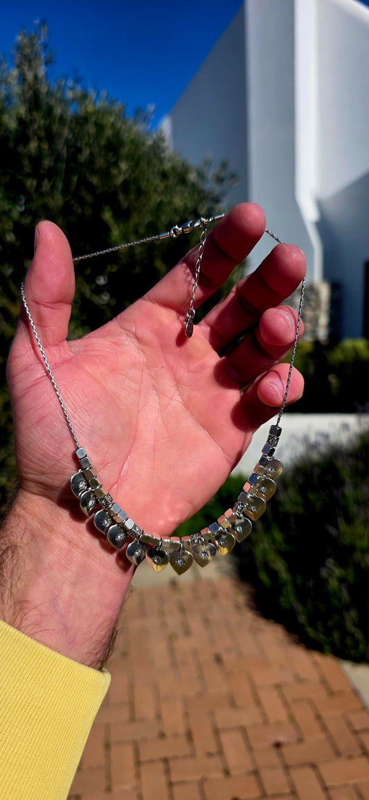 A beautifully feminine statement piece by renowned French jewellery house Gas Bijoux. This designer silver-plated necklace features a graceful row of heart dangles, each adorned with sparkling Swarovski crystal rhinestones in delicate starburst settings.