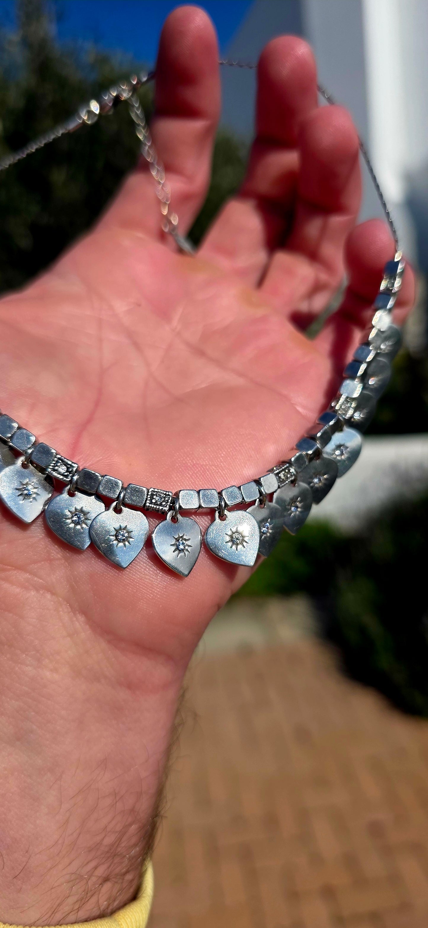 A beautifully feminine statement piece by renowned French jewellery house Gas Bijoux. This designer silver-plated necklace features a graceful row of heart dangles, each adorned with sparkling Swarovski crystal rhinestones in delicate starburst settings.
