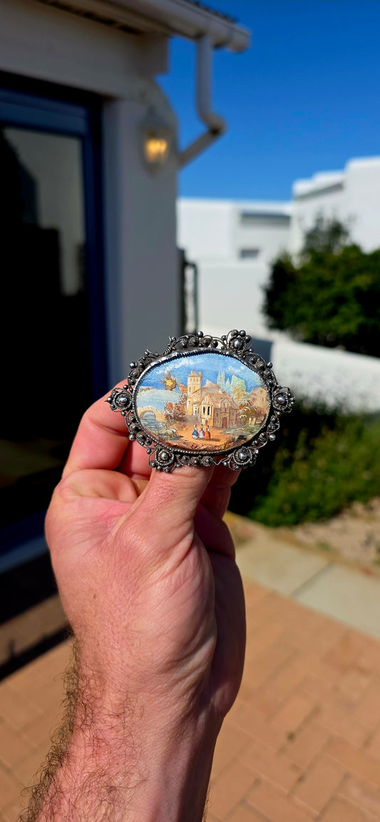 A truly beautiful and oversized antique Victorian-era sterling silver brooch, centred with a wonderfully detailed hand-painted miniature landscape scene, preserved beneath its original domed glass.