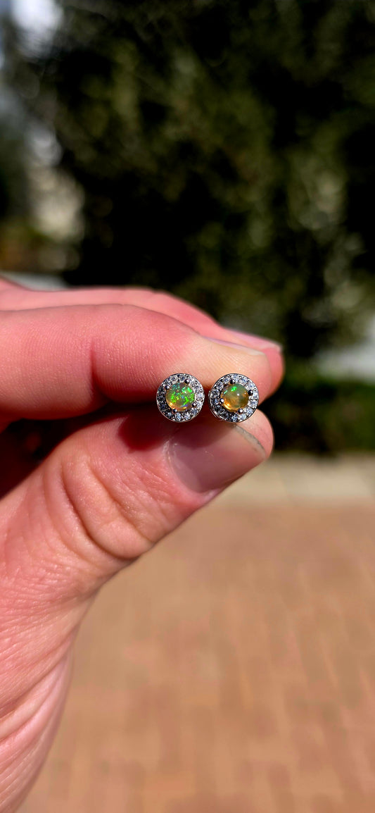 Small but absolutely magical! These beautiful stud earrings are crafted in solid sterling silver, each centred with a round natural Ethiopian opal cabochon, securely prong-set and surrounded by a delicate halo of sparkling CZ gemstones.