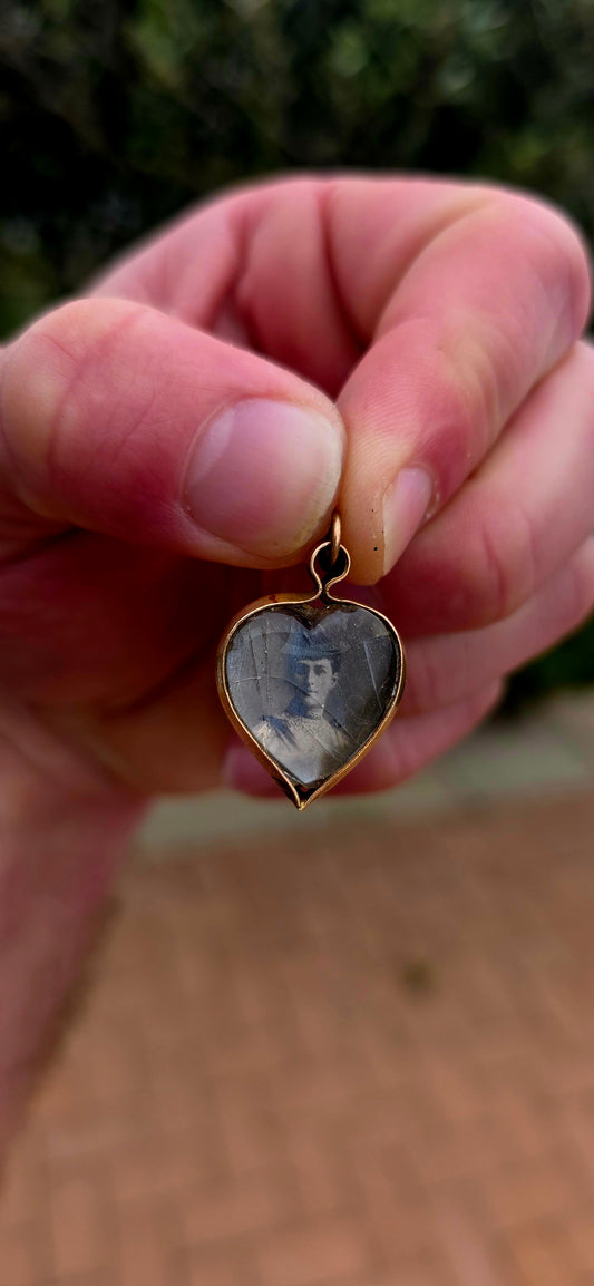 This antique Edwardian-era heart-shaped fob pendant features miniature photographic portraits of King Edward VII and Queen Alexandra, one displayed on either side beneath protective glass.