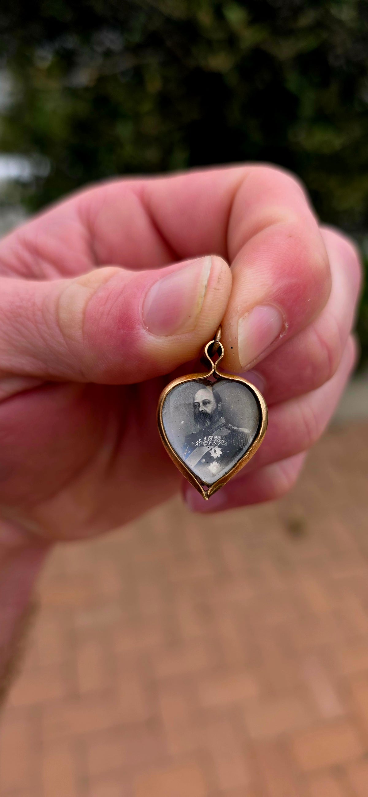 This antique Edwardian-era heart-shaped fob pendant features miniature photographic portraits of King Edward VII and Queen Alexandra, one displayed on either side beneath protective glass.