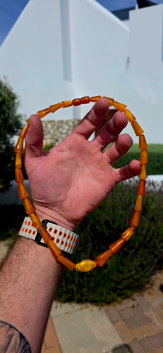 A striking Art Deco era necklace featuring a beautiful arrangement of elongated, graduated barrel-shaped beads in rich golden-orange, warm cognac and creamy butterscotch tones.