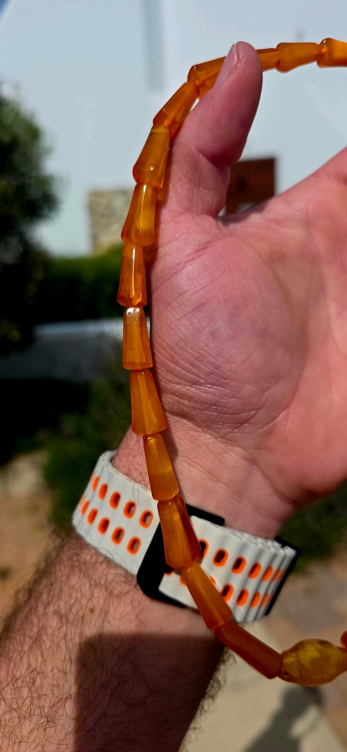 A striking Art Deco era necklace featuring a beautiful arrangement of elongated, graduated barrel-shaped beads in rich golden-orange, warm cognac and creamy butterscotch tones.