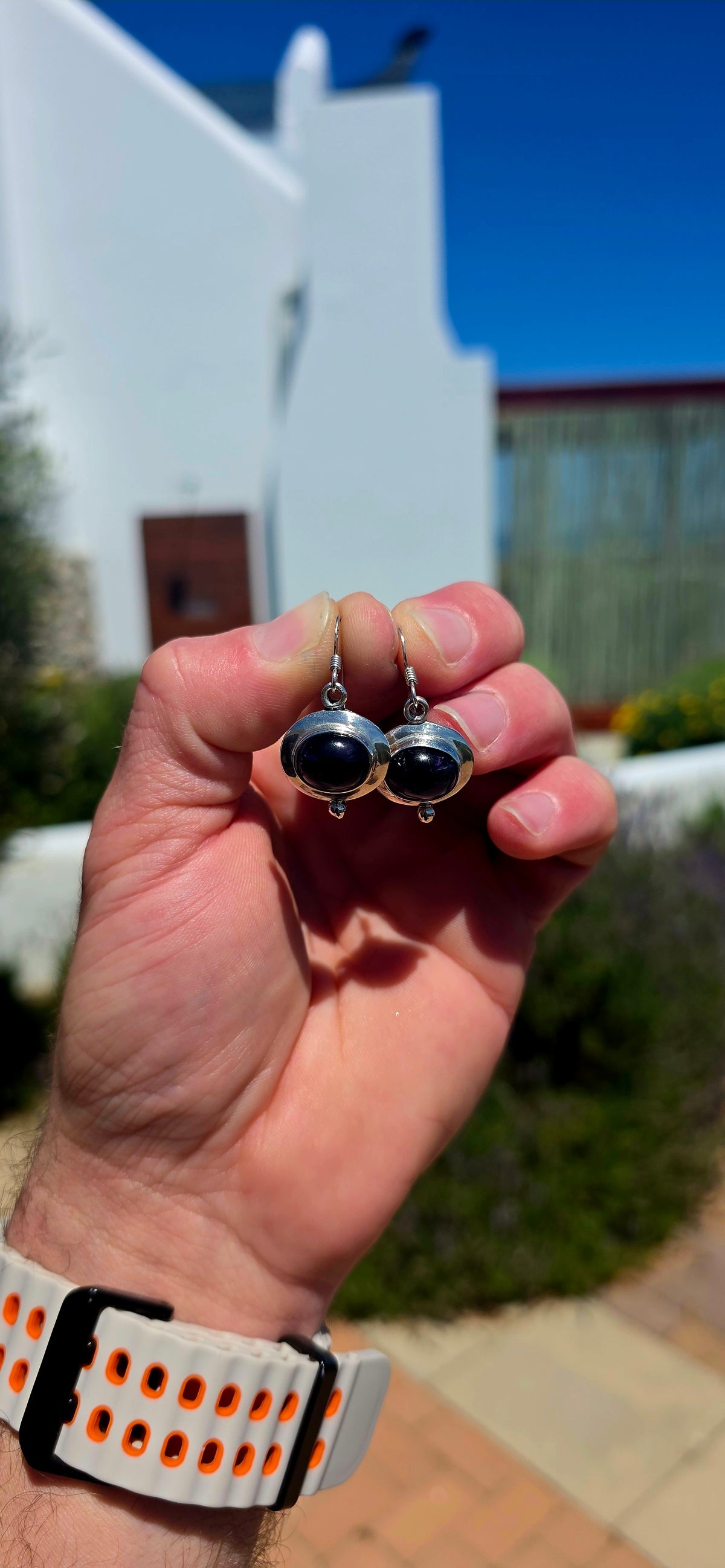 A beautiful pair of artisan-style sterling silver drop earrings featuring deep purple amethyst cabochons, beautifully complemented by sculptural silver settings.