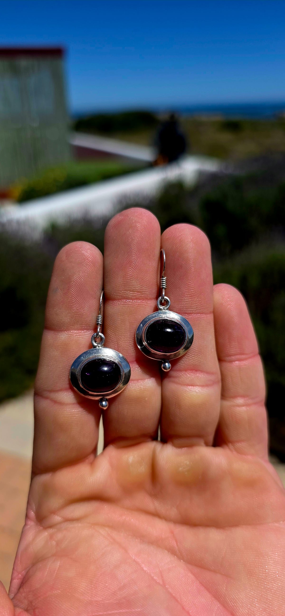 A beautiful pair of artisan-style sterling silver drop earrings featuring deep purple amethyst cabochons, beautifully complemented by sculptural silver settings.