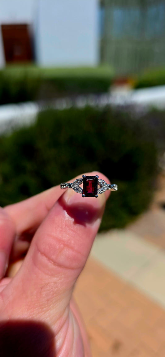 An elegant and beautifully feminine sterling silver solitaire-style ring, featuring a gorgeous emerald-cut rhodolite garnet at its centre, securely held in a classic four-prong setting.